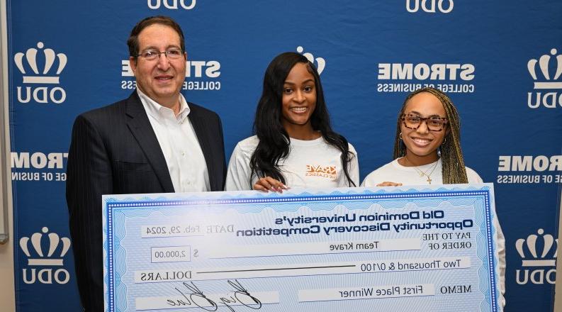 Three individuals pose with a large check